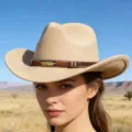 Beige wool felt western cowboy hat detail showing tribal woven band and golden feather. - Camel