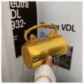 Elegante goldene Metall-Zylinder-Handtasche mit stilvollen Löwenkopf-Griffen und Kette. - Gold