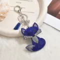 Detail shot of blue rhinestone fox keychain with metal clasp and tassel on white textured tray. - Sapphire Blue