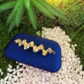 Detailed view of luxury blue frosted clutch featuring a striking golden wavy metal decoration. - Blue