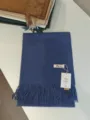 Detailansicht eines einfarbigen blauen Kaschmirimitat-Schals mit Fransen und Markenschild. - Denim-Blau