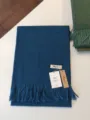 Detaillierte Nahaufnahme eines einfarbigen blauen Schals mit Quasten und dem Markenetikett. - Hain-Blau