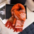 Close-up of orange jacquard winter scarf featuring elegant floral patterns and long fringe. - Orange