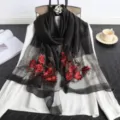 Primer plano detallado de un pañuelo negro transparente con bordado floral rojo y cuentas. - Negro