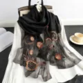 Detailansicht des schwarzen, transparenten Schals mit Blumenstickerei auf Bluse und Requisiten. - Schwarz