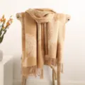 Detailed view of beige cashmere scarf featuring feather pattern and elegant tassels on wooden chair. - Camel