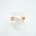 Detailansicht des goldenen Rings mit zentraler weißer Perle und klaren Baguettesteinen. - Ring / Acrylperlen / Gold