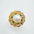 Dettaglio in primo piano del ciondolo di perle dorate con pietre verdi e cristalli brillanti. - Anello-Oro (Perla Naturale)