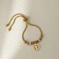 Detalle de pulsera de acero inoxidable dorada ajustable con colgante de cruz de diamantes y cuentas. - Cruz Dorada