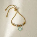 Detalle de pulsera de acero inoxidable dorado con abalorio de mal de ojo y cuentas brillantes. - Ojo Redondo Dorado