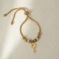 Elegante pulsera ajustable de acero dorado con abalorios de cristal y colgante de llave. - Dorado Llave