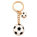 Portachiavi in lega dorata con due ciondoli da calcio in smalto nero e bianco per tifosi sportivi. - 25x29mm