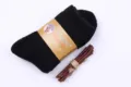 Detail shot of thick black wool winter socks with cardboard packaging and wooden prop. - Men's Black