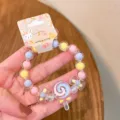 Close-up detail of children candy colored beaded bracelet featuring cute lollipop and bow charms. - Lollipop