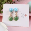 Close-up detail view of cute children clip-on earrings featuring green shell charms and blue beads. - Green Shell