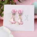 Close-up detail of cute pink heart and butterfly clip-on earrings on white display card. - Bow