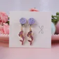 Close-up detail of cute purple glitter and mermaid clip-on earrings on a white card display. - Mermaid