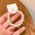 Detail view of white imitation pearl bracelet with cute carrot pendant, elegant jewelry close up. - Carrot