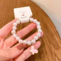 Close-up detail of pearl beaded bracelet with cute pink butterfly charm and hanging tag. - Butterfly