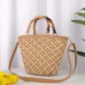 Detail view of woven straw shoulder bag featuring natural bamboo handle and brown strap. - Tan