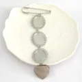 Detail view of retro stainless steel brooch blank with lace oval trays and heart pendant. - Three Panels / Silver