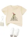 Détail de t-shirt graphique beige montrant l'imprimé mignon de grenouille à vélo et coton. - Abricot