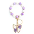 Llavero de cuentas de silicona moradas y blancas con dije de mariposa de metal. - Púrpura