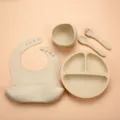 Baby silicone feeding set detail showing divided plate bowl bib spoon fork beige color. - Off White