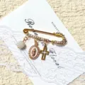 Vintage gold tone safety pin brooch featuring pearl bead, religious pendant and cross charm. - Gold