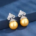 Primo piano dettagliato di eleganti orecchini di perle dorate con design superiore decorativo. - Orecchini a lobo / Oro