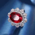 Detailed close-up of a stunning oval red gemstone ring with sparkling zircon halo cluster. - Ring / Ruby Red
