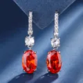 Close-up detail of elegant oval red gemstone drop earrings with sparkling cubic zirconia. - Orange Red Earrings
