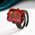 Radiant cut red gemstone ring featuring a bold black gold band and sparkling accent crystals. - Ring / Black Gold Orange Red