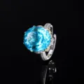 Close-up view of a large blue gemstone ring featuring sparkling pavé set rhinestones on band. - Adjustable Open / Aquamarine Blue Ring