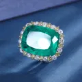 Stunning emerald cut green gemstone ring detail with sparkling crystal halo on blue fabric. - Ring / Emerald