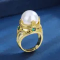 Detailopname van vintage gouden kroonring met grote witte parel en groene edelstenen dichtbij. - Wit