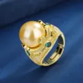 Detailopname van vintage vergulde ring met een grote gouden parel en groene accentstenen. - Goud