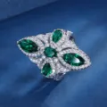 Primo piano dettagliato di un lussuoso anello a farfalla con pietra verde e brillanti zirconi. - Anello / Anello di Smeraldo