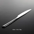 Stainless steel dinner knife detail shot, featuring a sleek round handle and beveled edge. - Dinner Knife