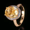 Dettaglio primo piano di anello di lusso con gemma ovale gialla e contorno di zirconi blu. - Taglia US 6 / Strass Giallo Taglio Fiore di Ghiaccio