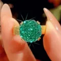 Primo piano di un elegante anello con gemma preziosa da 12mm e finitura dorata spazzolata. - Taglia US 6 / Verde Paraiba