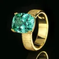 Primo piano dettagliato di un anello con gemma verde taglio cuscino e fascia d'oro testurizzata. - Taglia US 6 / Verde Paraiba