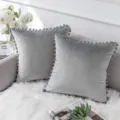 Graues Samtkissen mit Pompons Detail auf dem Wohnzimmersofa in gemütlicher Deko Szene. - Grau