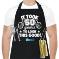 Vista detallada del delantal de cocina negro con estampado divertido y bolsillos. - Estampado 50 Cumpleaños / Negro