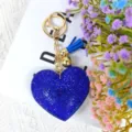 Gros plan détaillé du porte-clés cœur en strass bleu avec quincaillerie dorée et pompon. - Bleu