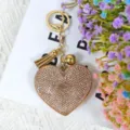 Gros plan détaillé d'un porte-clés cœur en strass étincelant avec pompon et breloque dorés. - Multicolore