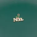 Close-up detail of a gold-tone metal NOEL Christmas charm pendant with green leaves and red berries. - Christmas Series / 12# Letter