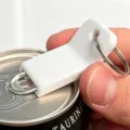 Close-up detail showing white plastic pull tab can opener keychain in use on a beverage can. - White