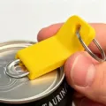 Yellow plastic can opener keychain close-up detail, portable ring pull opener tool for drinks. - Yellow