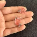 Nahaufnahme von 12 mm großen rosa Kristallanhängern in Herzform, zur Größenangabe in der Hand. - 12x6mm / Wassermelonenrot